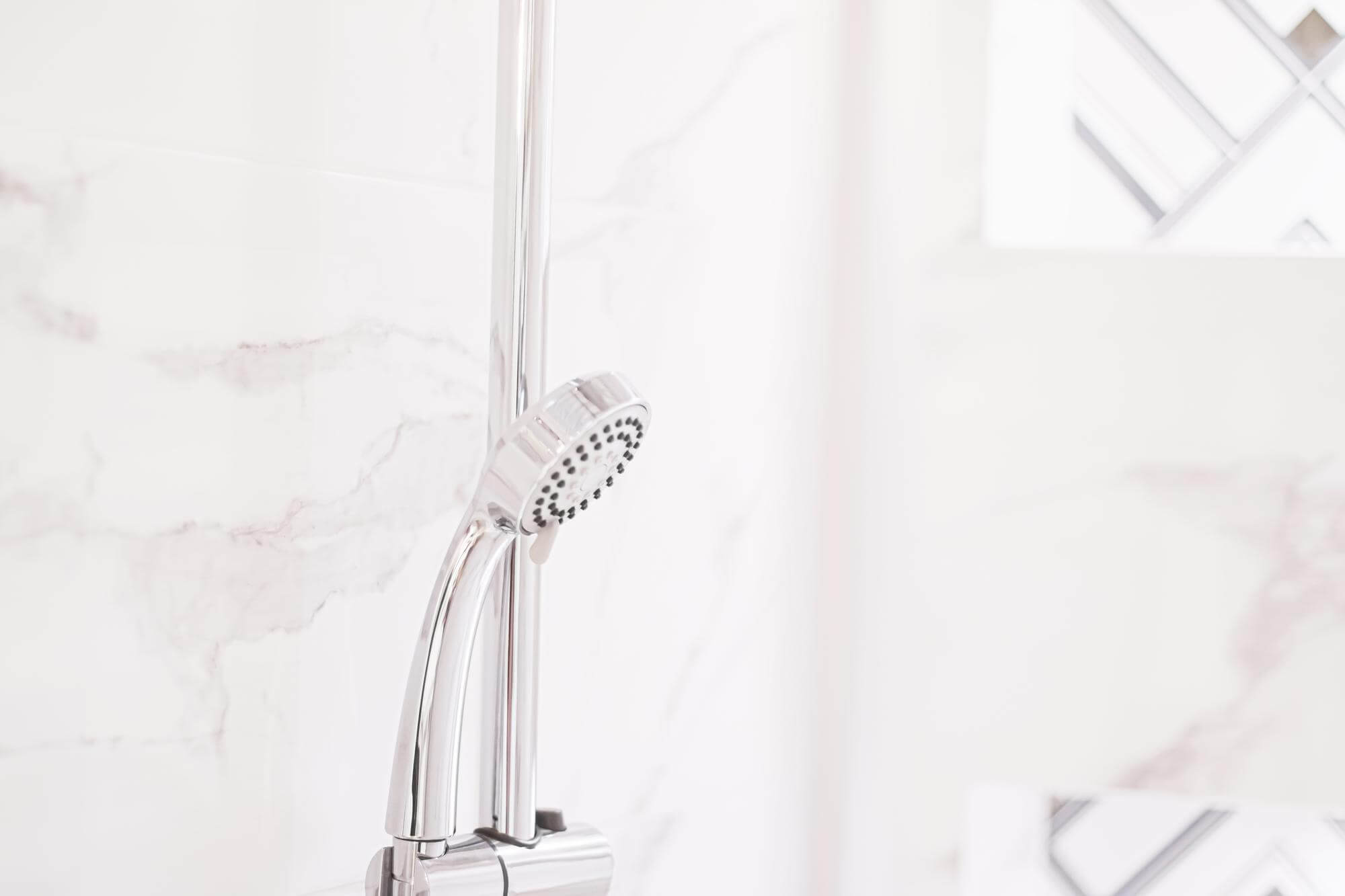 Krominen käsisuihku kiinnitetty vaalean marmorinväriseen kylpyhuoneeseen.